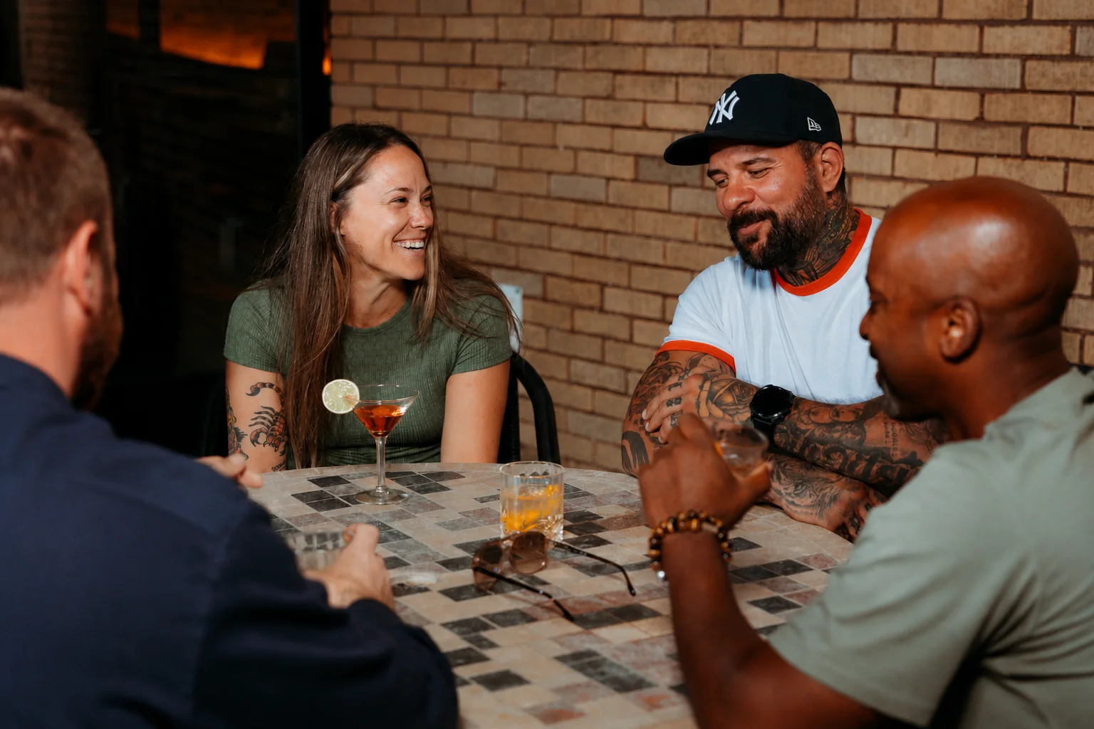 Four friends around a courtyard table with cocktails