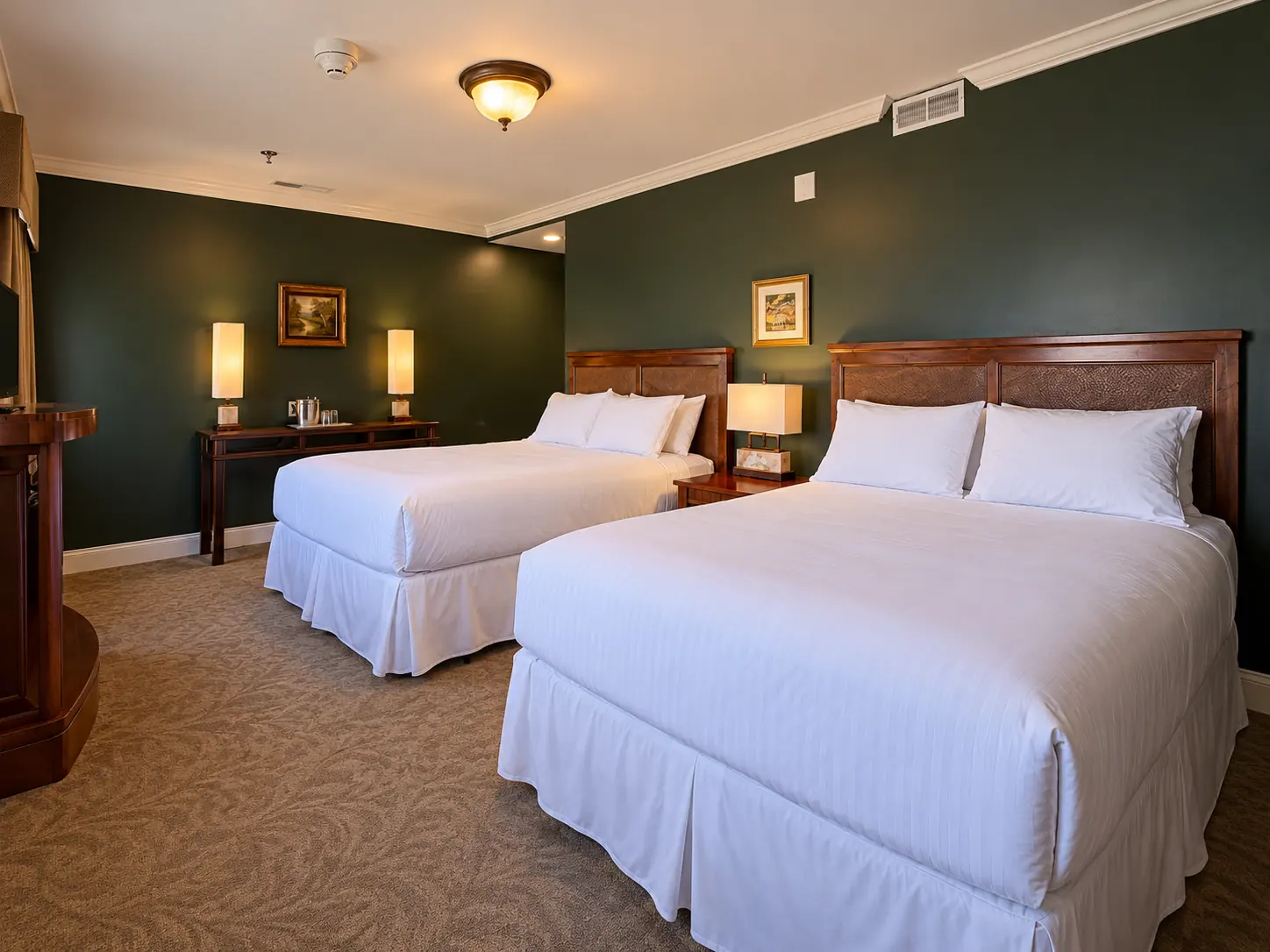 Two queen beds with wood headboards against a green wall